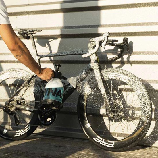 Zwarte racefiets, bespoten met wit schuim, door een hand met een spuitfles.