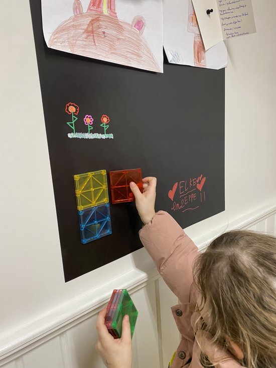 Une fille porte une veste et place des blocs magnétiques sur un tableau noir avec un dessin.