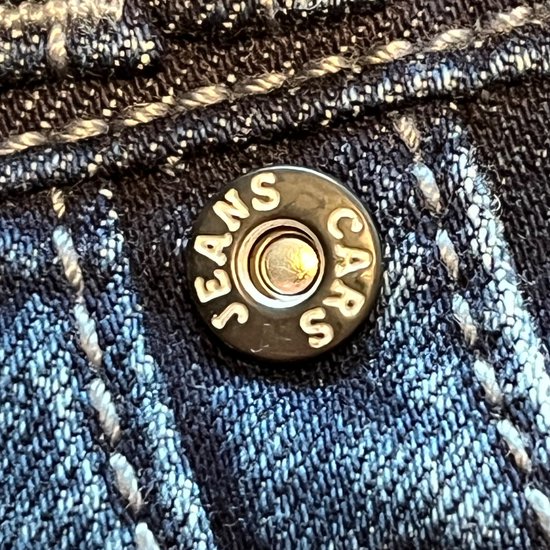 Knop met "CARS JEANS" op een donkerblauwe spijkerbroek.