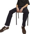 Jongen zit op een stoel, toont zijn donkergrijze cargo broek en bruine sneakers.