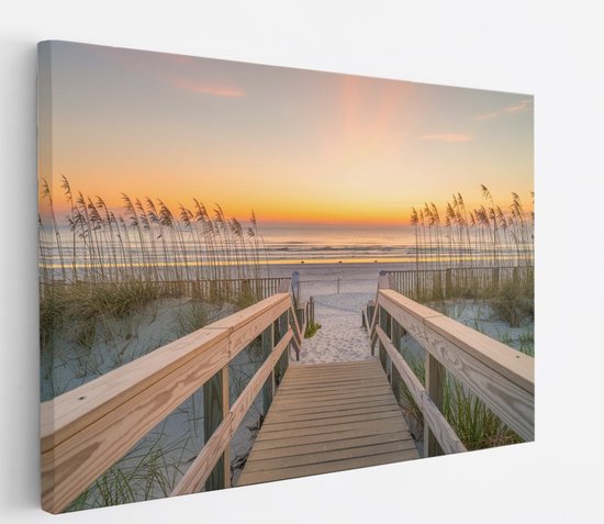 Een houten looppad over zandduinen naar het strand bij zonsondergang, omringd door wuivend gras.