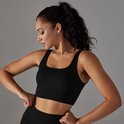 Model in zwart sporttopje met vierkante halslijn en racerback, die het kledingstuk aanpast.