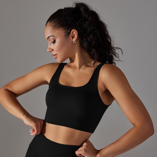 Model in zwart sporttopje met vierkante halslijn en racerback, die het kledingstuk aanpast.