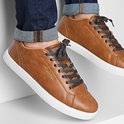 Voeten in bruine Jack & Jones sneakers met witte zolen en donkergrijze veters, gecombineerd met spijkerbroek.