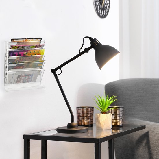 Een zwart metalen gaas tijdschriftenrek met tijdschriften, naast een bureaulamp.
