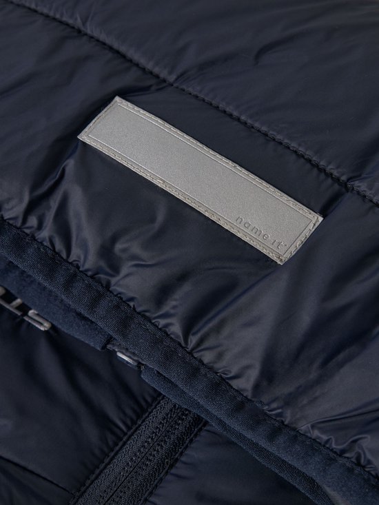 Detail van de donkerblauwe gewatteerde jas met zilverkleurig label 'name it'.