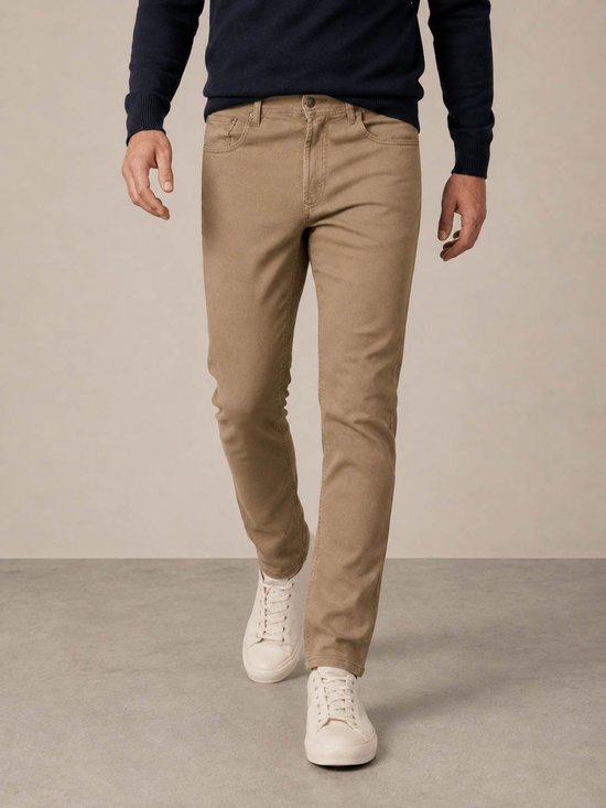 Model draagt een moderne bruine jeans met een donkerblauwe trui en witte sneakers.