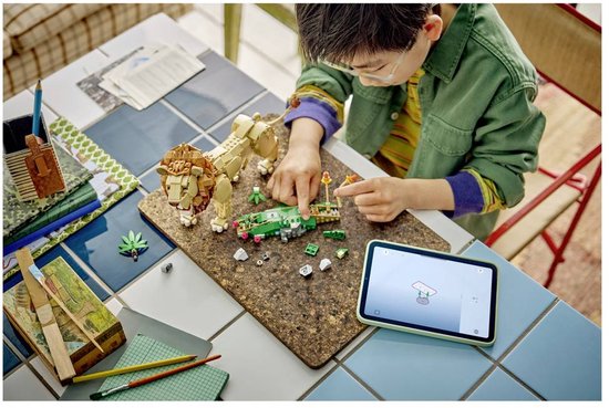 Jongen met bril bouwt met LEGO stenen een leeuw en voertuig, met een tablet ernaast.