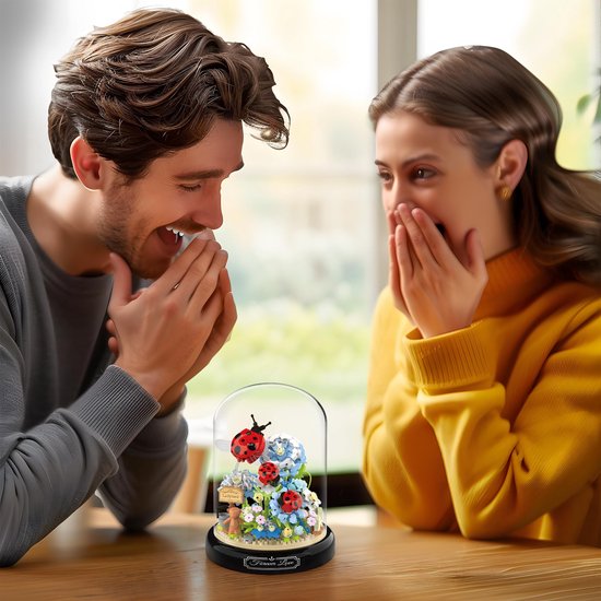 Man en vrouw kijken verrast naar een glazen stolp met micro mini blokjes, bloemen en lieveheersbeestjes.