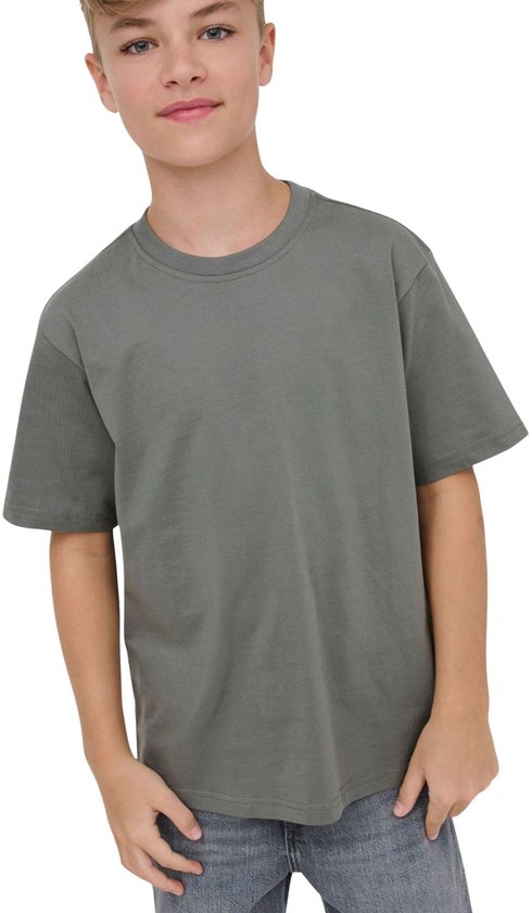 Jongen met blond haar draagt een effen donkergrijs T-shirt en spijkerbroek, lachend naar de camera.