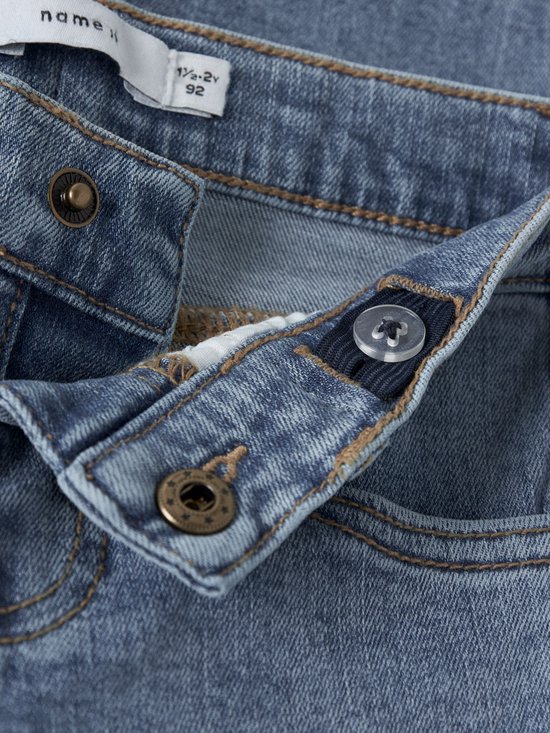 Detail van de knoopsluiting en het label van een blauwe spijkerbroek.