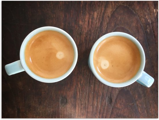 Twee lichtblauwe kopjes gevuld met koffie met crèmige schuim, op een donkere houten tafel.