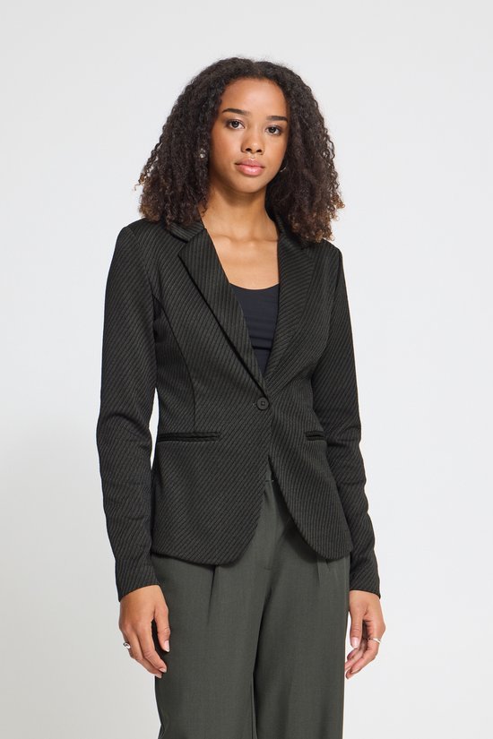 Model in een zwarte blazer met diagonaal patroon en één knoop, gecombineerd met een donkergrijze pantalon.