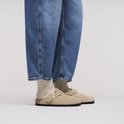 Een persoon draagt beige suède Birkenstock Boston muilen met jeans en sokken.