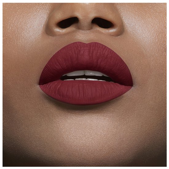 Matte bordeauxrode lippenstift op een mond, met witte tanden zichtbaar.