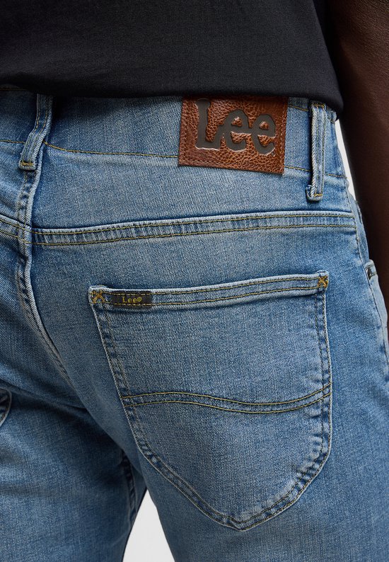 Detail van de achterkant van een lichtblauwe spijkerbroek met een bruin lederen Lee-patch en een klein Lee-logo.