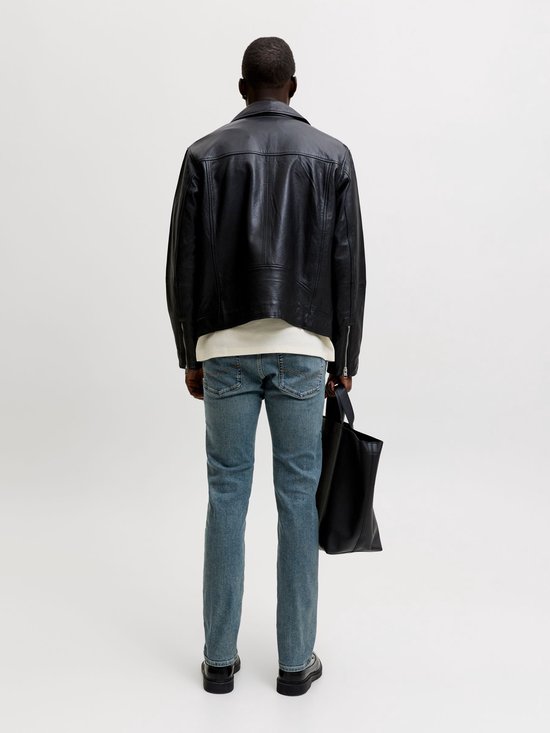 Man draagt blauwe slim fit jeans van Jack & Jones, zwarte leren jas, wit shirt en zwarte schoenen.