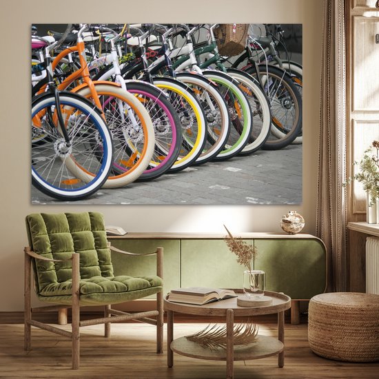 Une rangée de vélos colorés avec des jantes orange, bleues, blanches, roses et jaunes, au-dessus d'une commode et d'une chaise.