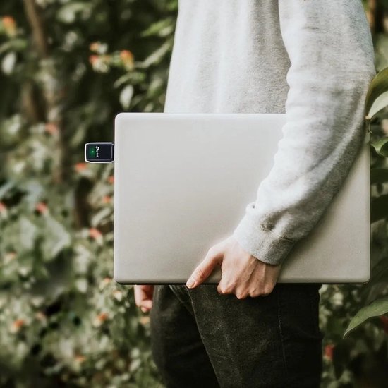 Een persoon houdt een laptop vast met een zwarte TP-Link Archer T3U WiFi-adapter aangesloten op de USB-poort.