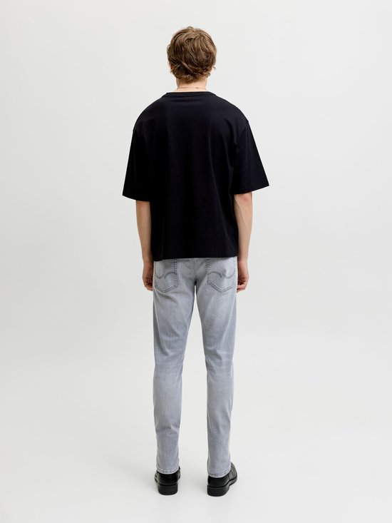 Man in een zwart T-shirt en lichte grijze slim fit jeans, achterkant zichtbaar.