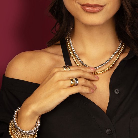 Vrouw draagt gouden en zilverkleurige kettingen met balletjes en bijpassende ringen.