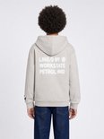 Jongen draagt lichtgrijze hoodie met tekst op de rug en donkere jeans. De capuchon is op.
