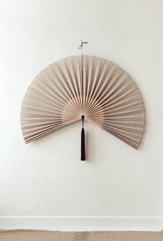 Un éventail décoratif en bambou avec des rayures noires et un pompon noir sur le mur.