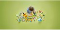 Kind met LEGO Duplo trein, station, voertuigen en accessoires op groene achtergrond.