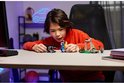 Garçon en pull orange construisant du LEGO Fortnite avec les personnages Peely et Sparkplug, incluant un dragon et une mine.
