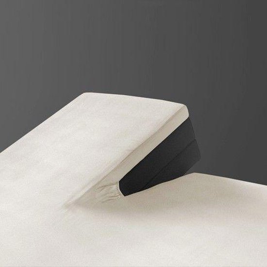 Gedetailleerde hoek van een matras met een crème splittopper hoeslaken en deels zichtbaar donker matras.
