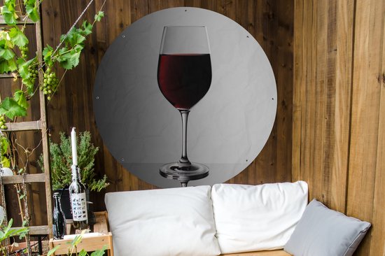 Rond tuinposter met glas rode wijn op grijs witte achtergrond, hangend aan houten muur naast bank.