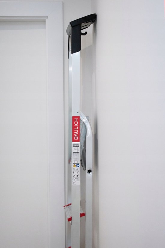 De opgevouwen aluminium huishoudladder staat tegen een witte muur.