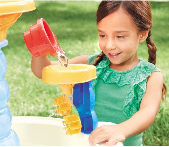 Een meisje met een groen shirt met ruches giet water in een gele trechter aan een waterpark.
