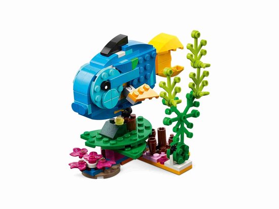 Een blauwe LEGO vis met een gele rugvin en staart, zittend op een groene ondergrond met roze bloemen en planten.