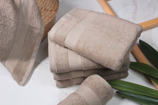 Stapel beige handdoeken met ribbelrand. Een deel van de handdoeken ligt naast een mand en groene bladeren.
