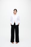 Model met witte blouse met lange mouwen, een zwarte broek met wijde pijpen en een ceintuur.