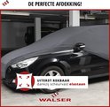 Zwarte auto met grijze, uiterst rekbare autohoes van elastisch materiaal, in een garage.