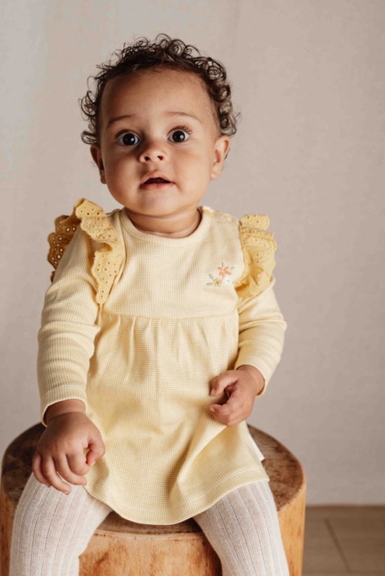 Baby in een geel geruit jurkje met ruches en bloemenapplicatie, wit gebreide maillot.