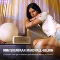 Crème Marshall speaker op een tafel naast een vrouw. Onmiskenbaar Marshall-geluid.