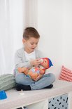 Jongen geeft BABY born pop flesje. Zittend op een bankje met witte lakens.