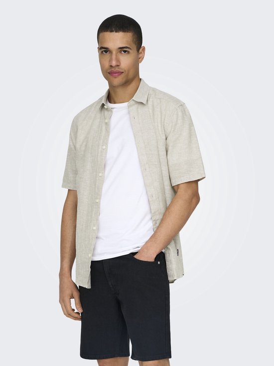 Man met korte mouwen, lichtbeige linnen mix overhemd, witte t-shirt, zwarte korte broek.