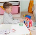 Jongen voert BABY born Jonas pop, zittend in een roze stoel, met een lepel uit een schaaltje.