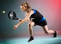 Vrouw in zwart sporttenue met blauwe accenten speelt padel met een zwart racket.