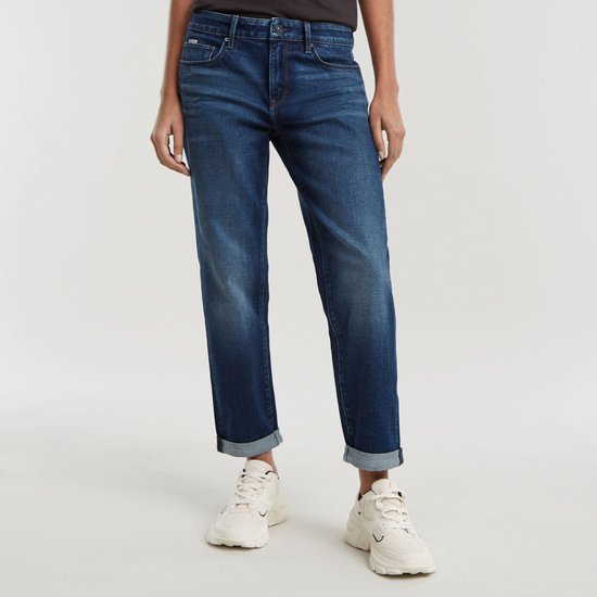 Model draagt een donkerblauwe jeans met omgeslagen broekspijpen en witte sneakers.