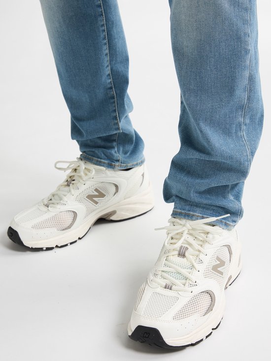 Lichtblauwe sneakers met witte mesh details en een zilverkleurige N-logo. Gedragen door iemand in een spijkerbroek.