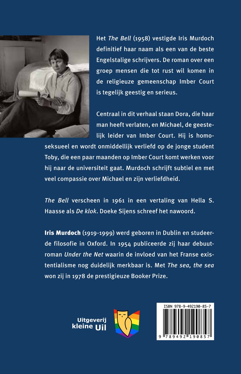 Iris Murdoch in een wit blouse en bruin jasje, zittend met gekruiste benen.
