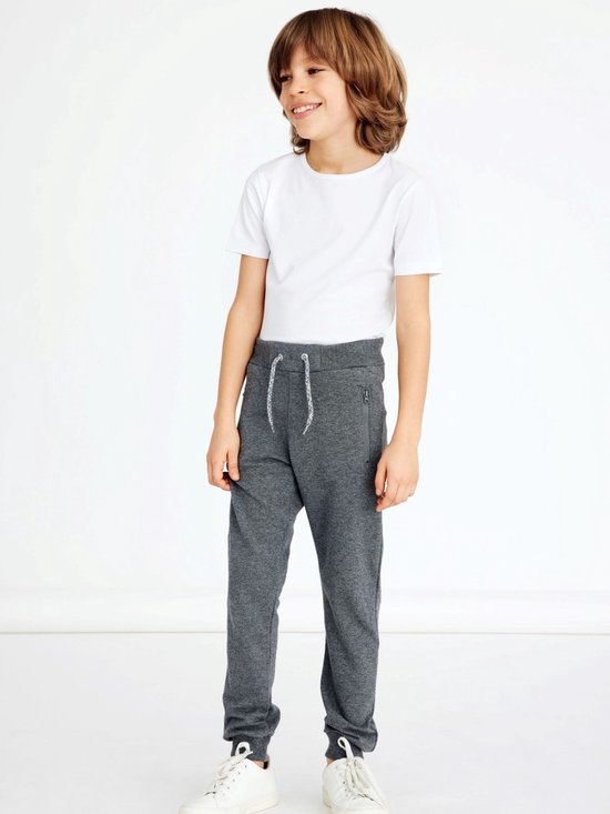 Jongen draagt een grijze joggingbroek met witte t-shirt en witte sneakers.