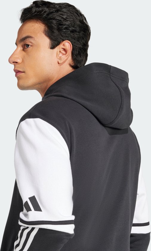 Man met een donkergrijs sweatshirt met witte mouwen en Adidas-strepen op de mouwen.