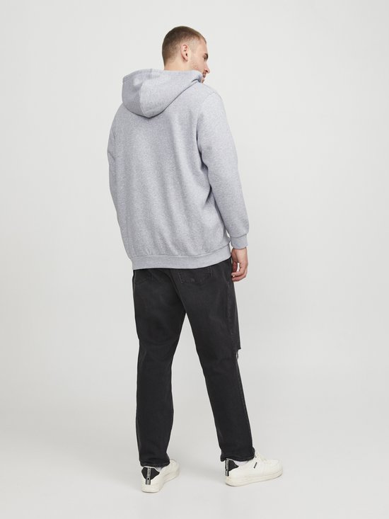 Man draagt een lichtgrijze hoodie met rits, achterkant zichtbaar, met een zwarte jeans.