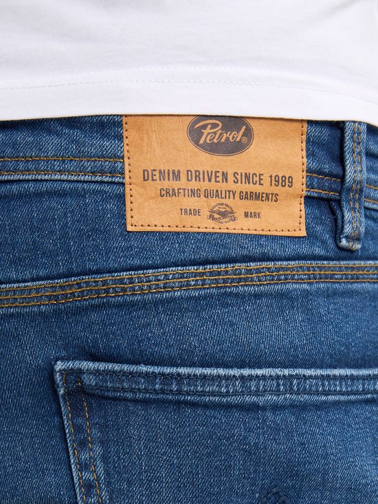 Detail van de achterkant van een spijkerbroek met een bruin leren label met de tekst 'Petrol Industries Denim Driven Since 1989'.